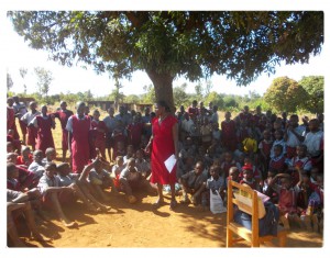 De leerkracht stelt spreker Lawrence van JAWA voor. Enkele klassen hebben zich verzameld onder een boom om te luisteren.