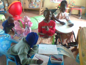 Vier kinderen binnen in JAWA. Twee van hen kleuren in kleurboeken.
